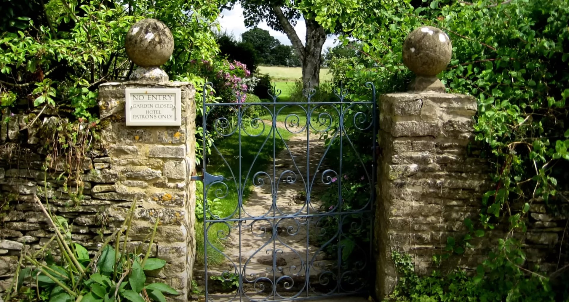 Ornate garden gate entrance with stone pillars and mature landscaping